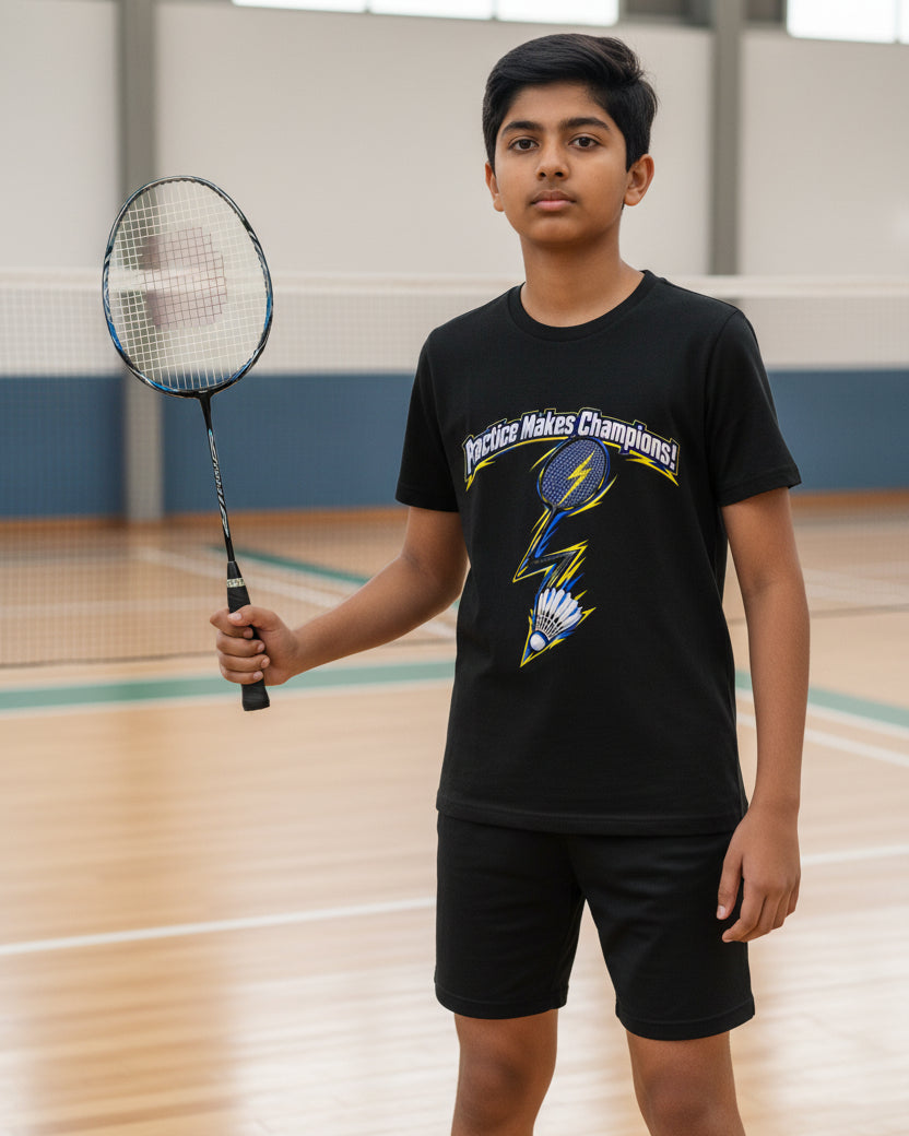 A black short-sleeve kids' t-shirt featuring a graphic of a badminton racket and shuttlecock with a lightning bolt, under the text 'Practice Makes Champions!'.